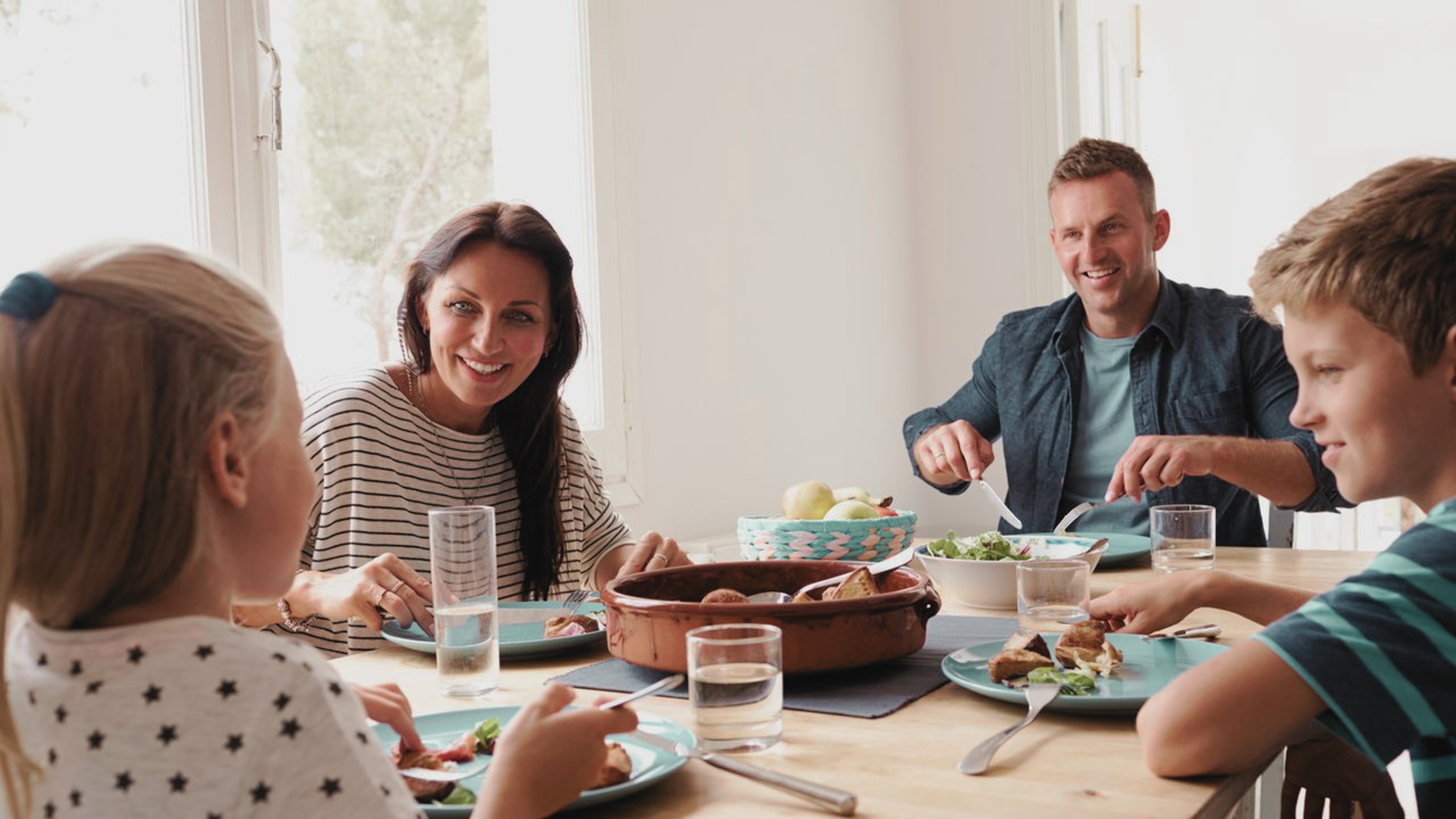 Une famille réunie autour d'une table, partageant un repas. Des enfants et des adultes affichent des sourires, créant une atmosphère chaleureuse et conviviale.