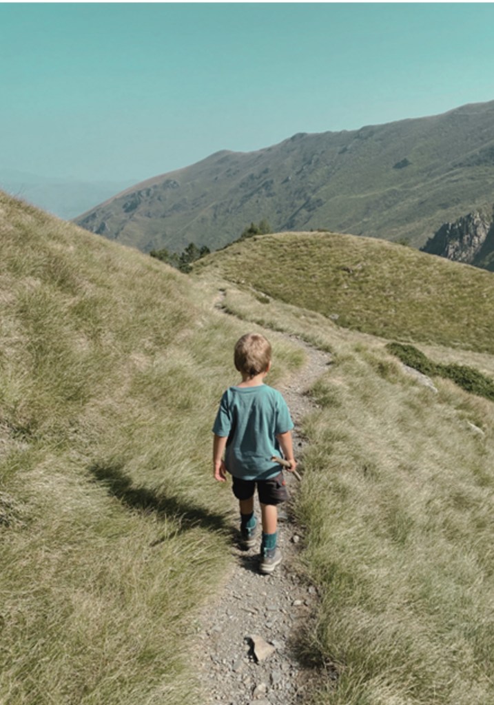 Un enfant marchant sur un sentier de montagne entouré d'herbe verte et de collines.