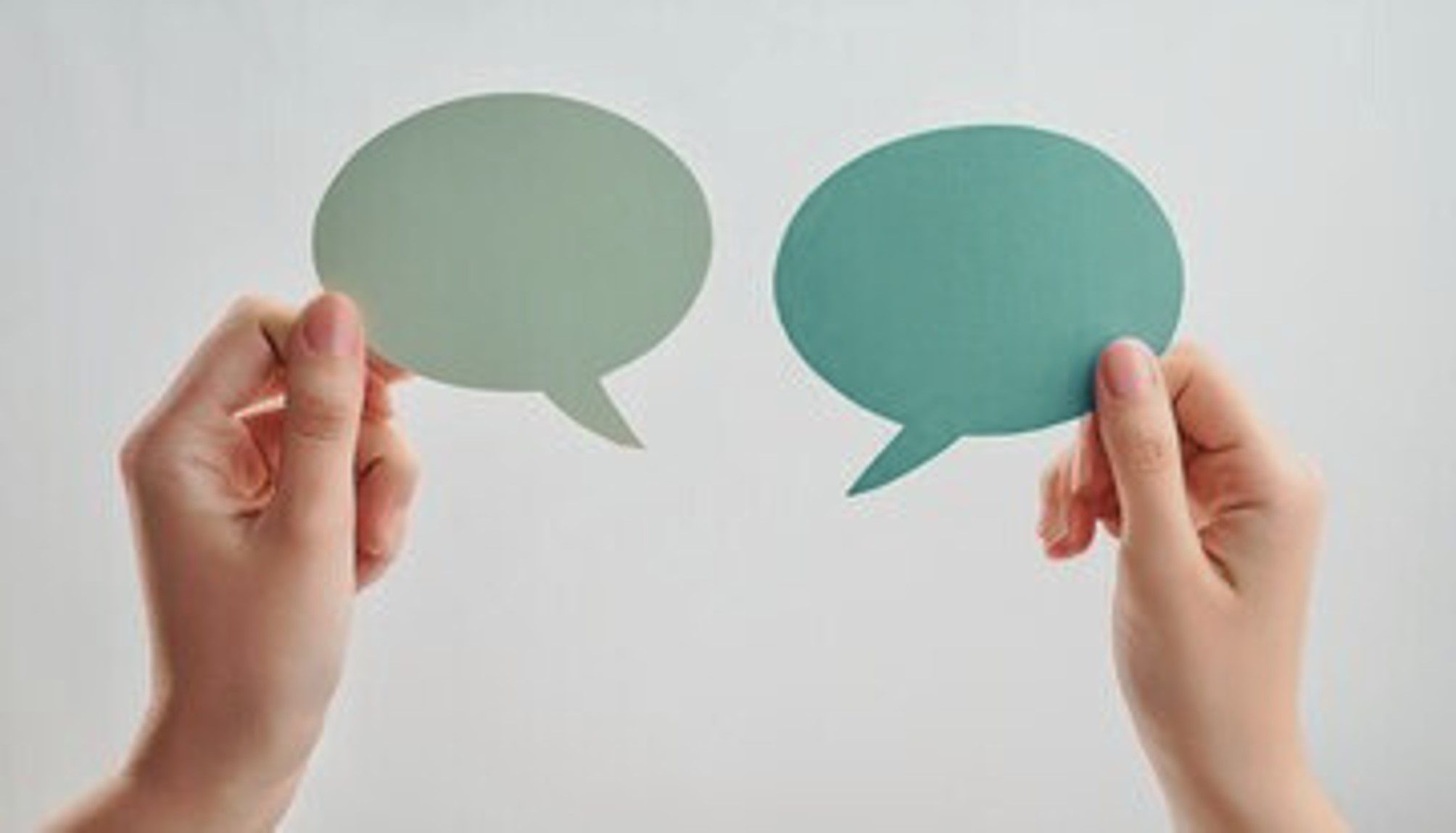 Deux mains tenant des bulles de dialogue en papier, l'une de couleur verte et l'autre turquoise, sur un fond neutre.