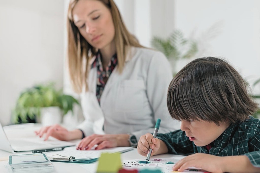 Une thérapeute aide un jeune garçon à dessiner sur une feuille pendant une session d'apprentissage à un bureau.